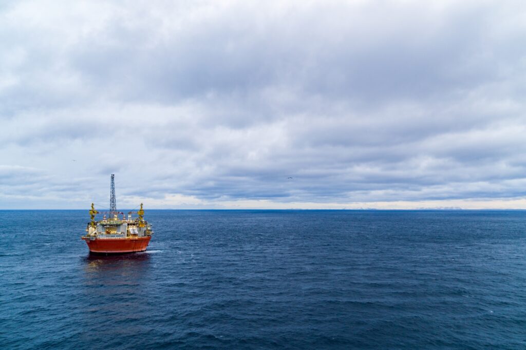 Oil platform in calm sea. Cloudy sky. Mountains in a distance. Photo.